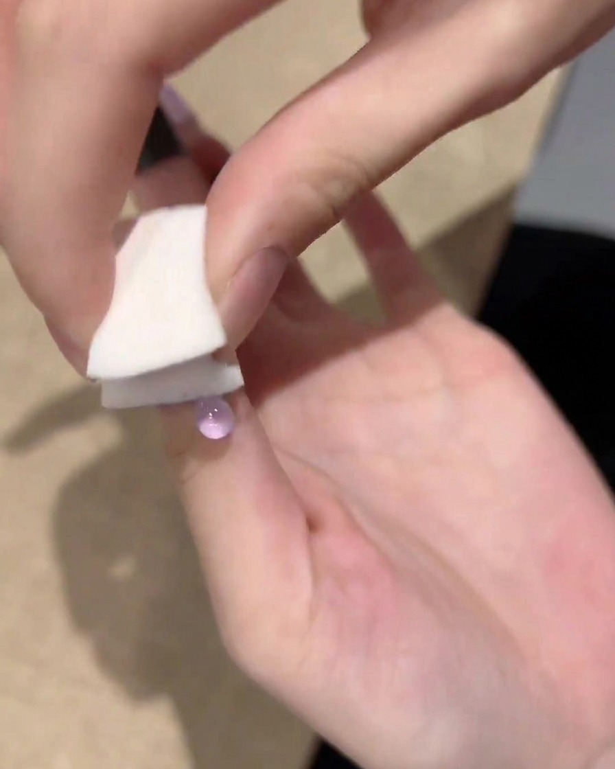 Une main utilisant une petite éponge blanche pour tapoter et estomper le vernis gel violet de la pointe de longle vers le centre.