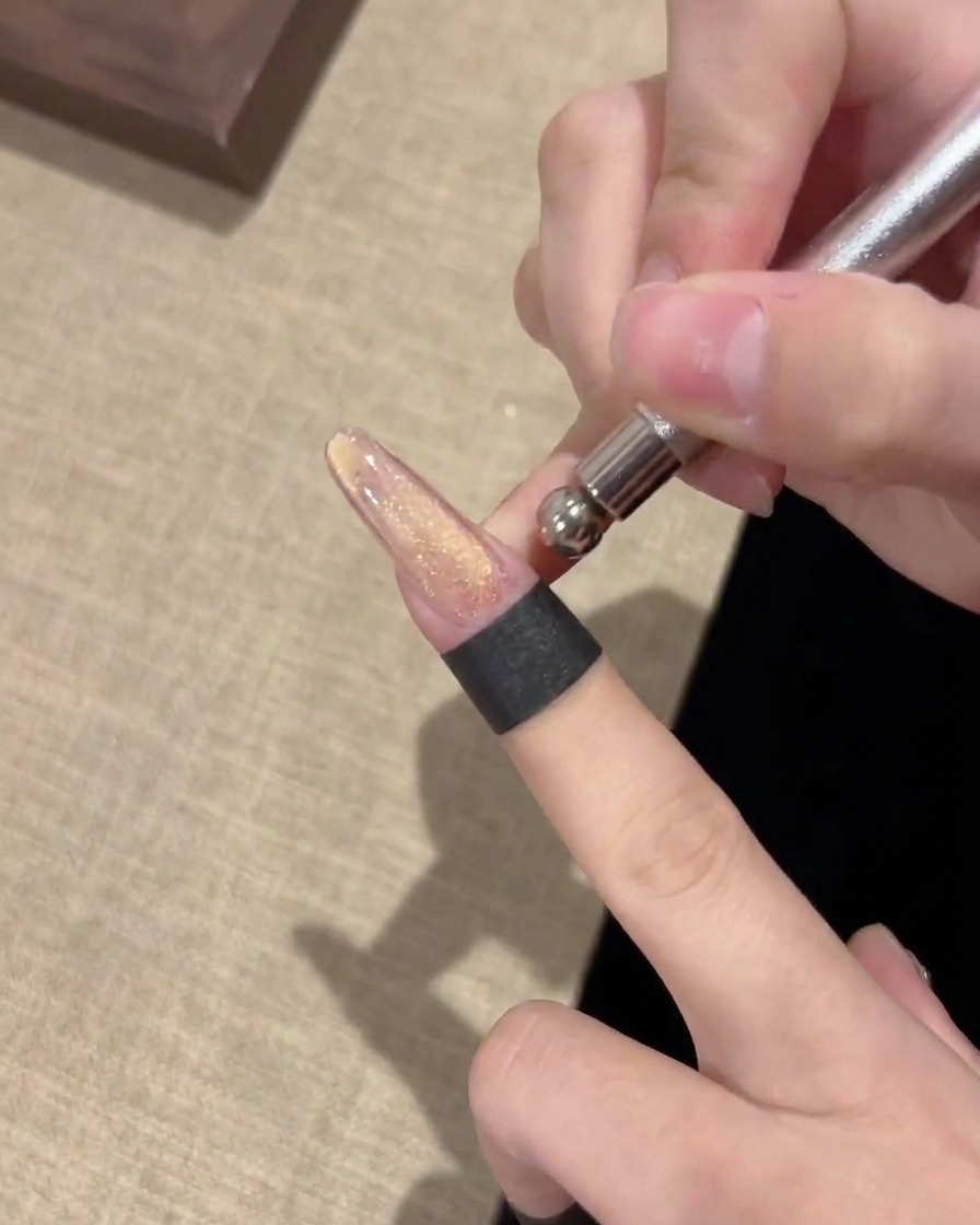 Gros plan sur un outil aimanté métallique maintenu horizontalement au-dessus dun ongle pour manipuler les particules de gel magnétique.