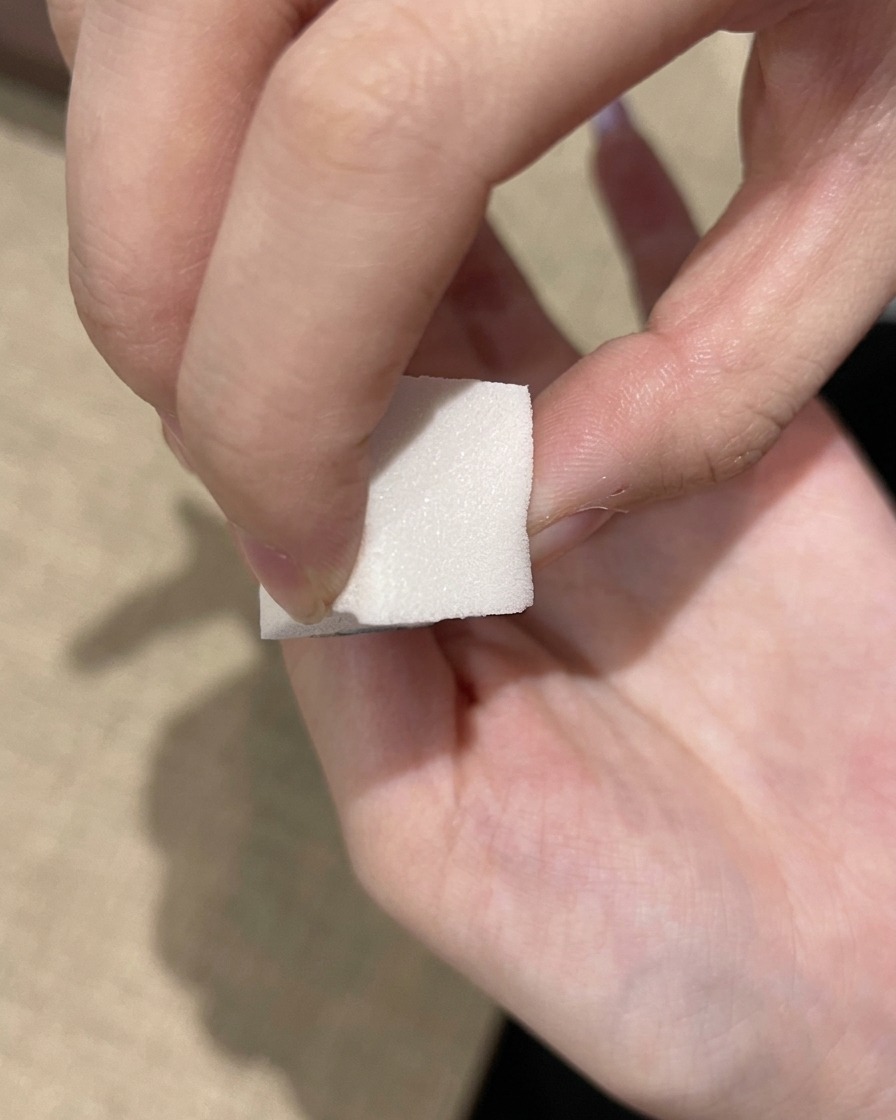 Une éponge à maquillage blanche tapotant un vernis gel violet foncé sur le bord libre dun ongle.