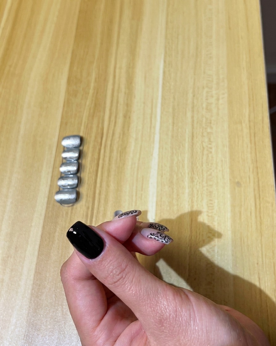 Un pinceau appliquant une fine couche de vernis gel noir sur un ongle naturel.