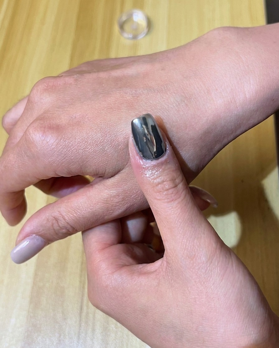 Un applicateur mousse frottant du pigment chrome argenté sur un ongle peint en gel noir.