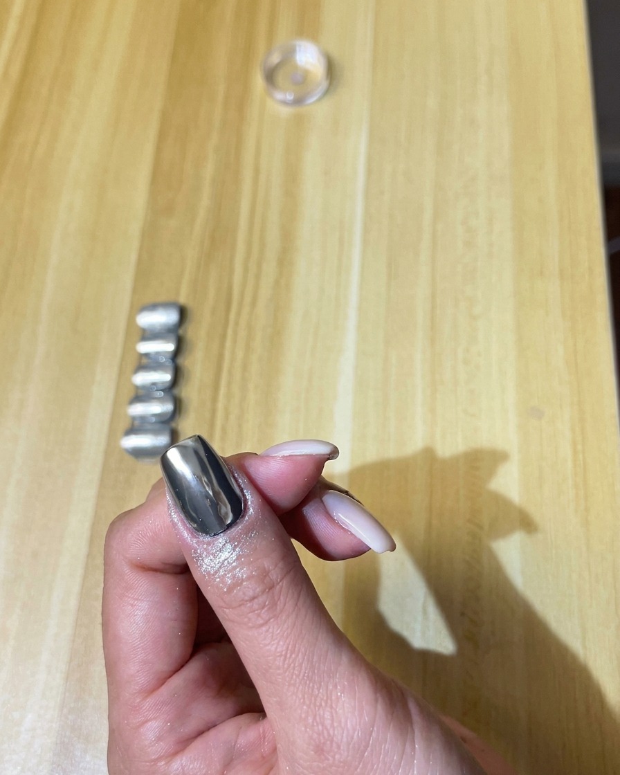 Un pinceau de maquillage souple retirant doucement la poudre chrome en surplus de longle.