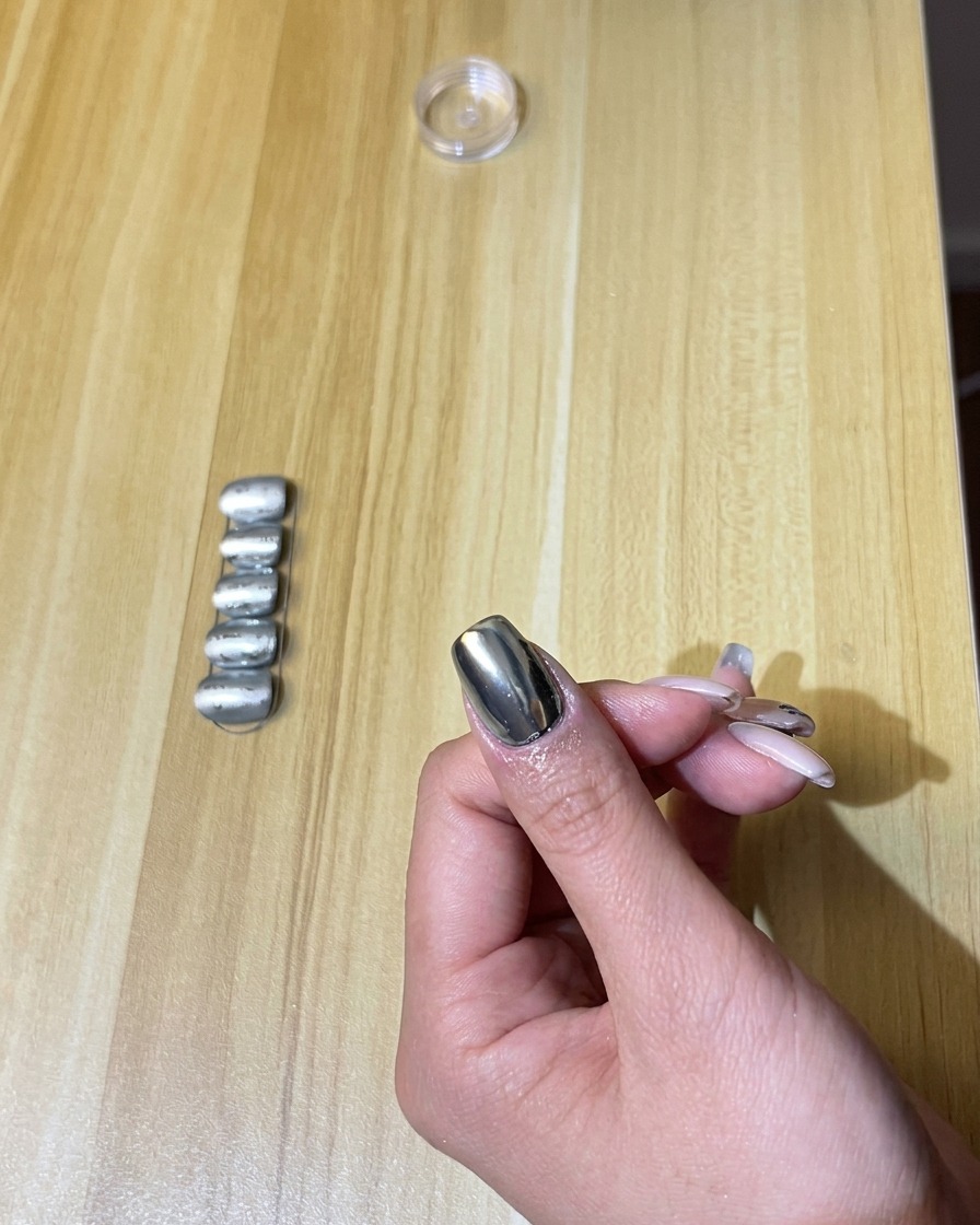 Une main avec des ongles chromés sous une lampe UV/LED allumée.