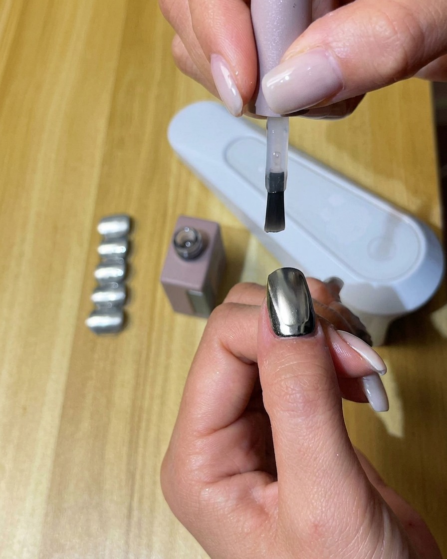 Une main aux ongles recouverts de top coat mat sous une lampe UV/LED.