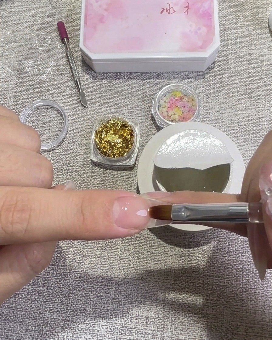 Une main utilisant un pinceau gel plat pour appliquer une couche de gel dur transparent.