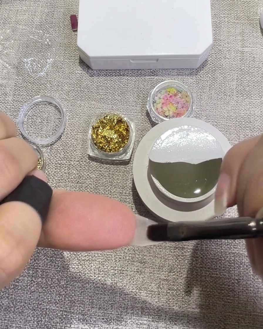 Une pince déposant de petits pétales de fleurs séchées colorées sur un ongle couvert de gel humide.