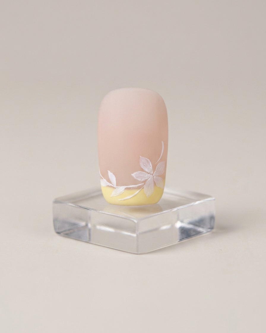 Un pinceau applique une fine couche de base coat nude sur longle naturel.