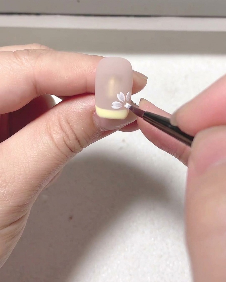 Gros plan sur lapplication dun blooming gel blanc créant un pétale sur une base nude.