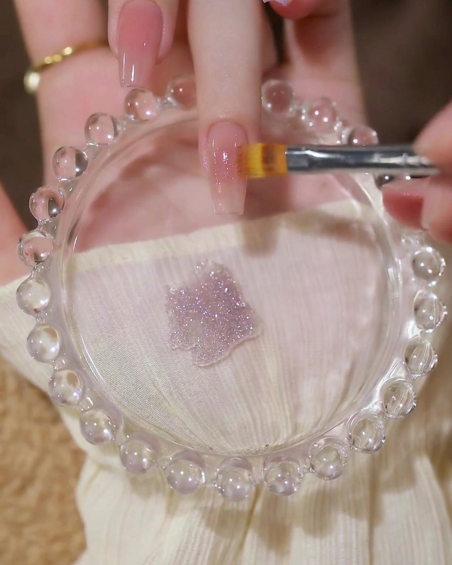 Pinceau appliquant une couche de gel pailleté translucide sur une base nude.