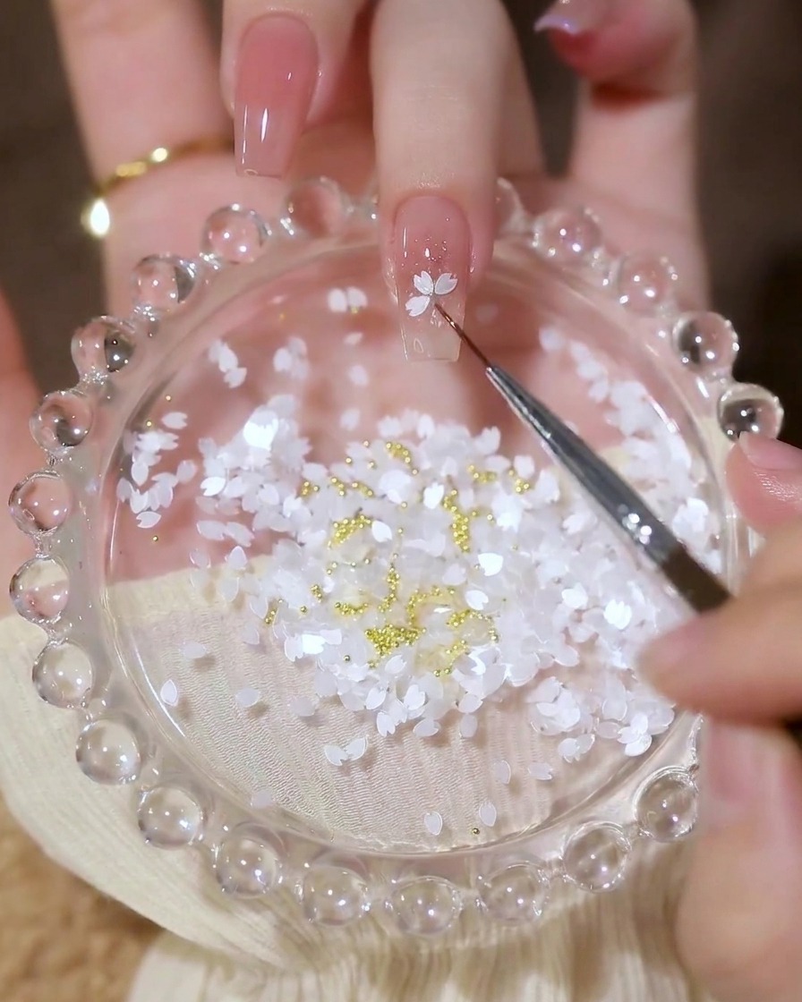 Gros plan dun pinceau de détail plaçant des sequins en forme de pétales blancs pour former une fleur.