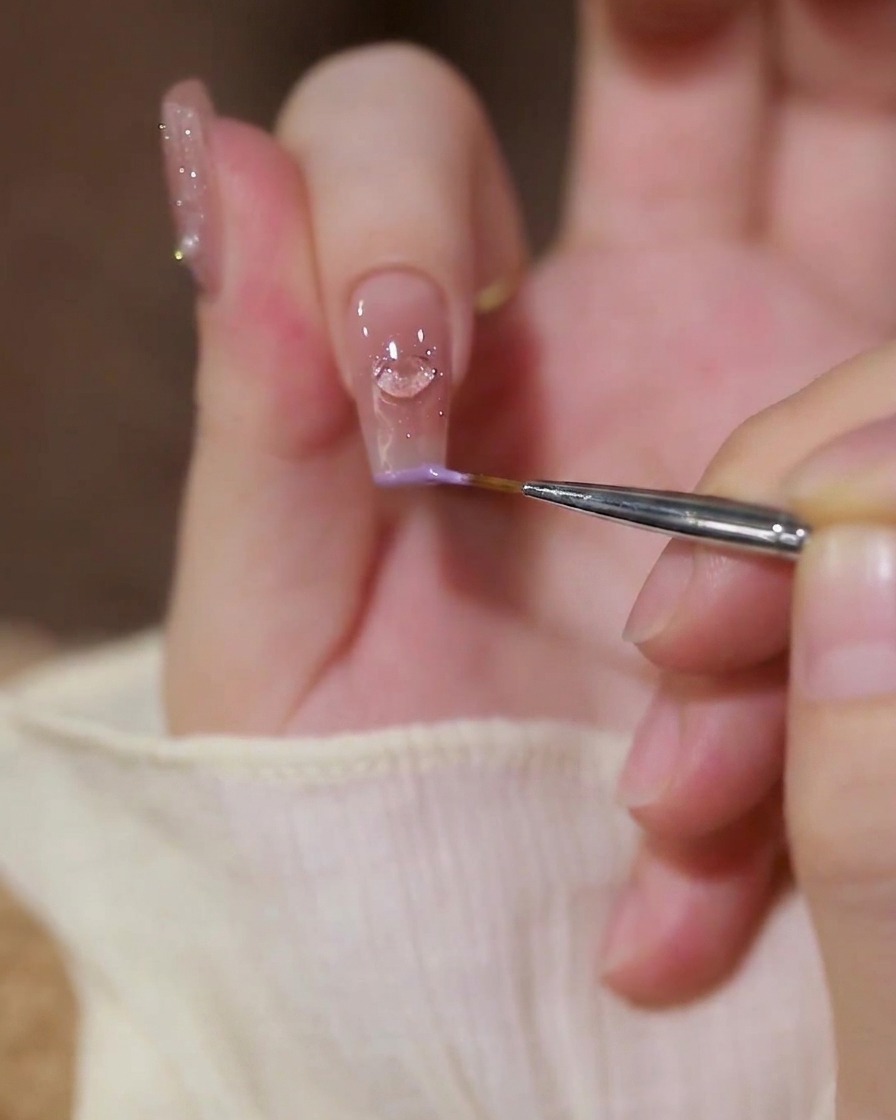 Gros plan dun pinceau liner appliquant du gel violet pastel sur le bord de lindex.