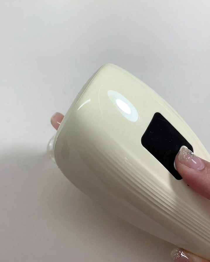 Une main tenant une petite lampe UV/LED portable directement au-dessus dun ongle verni en nude pour catalyser.