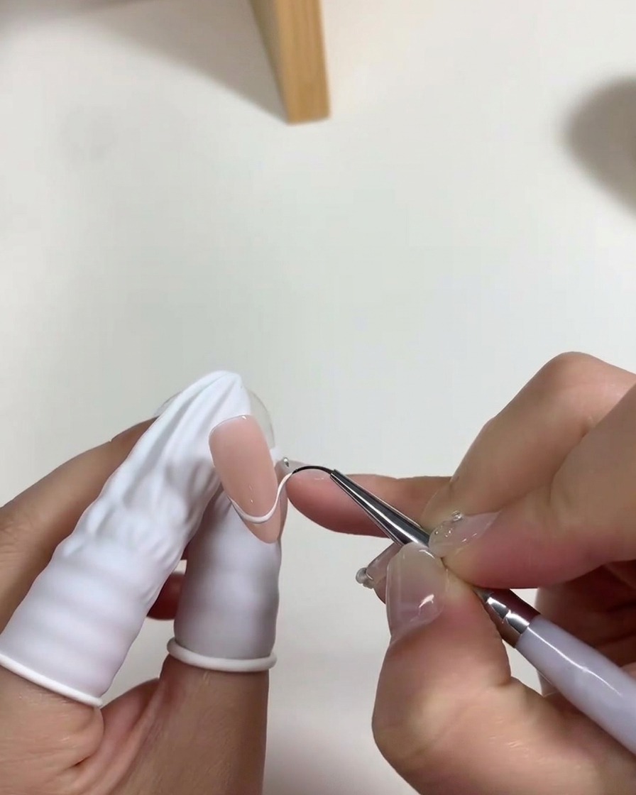 Un pinceau appliquant une fine couche de vernis gel blanc laiteux sur la plaque de longle.