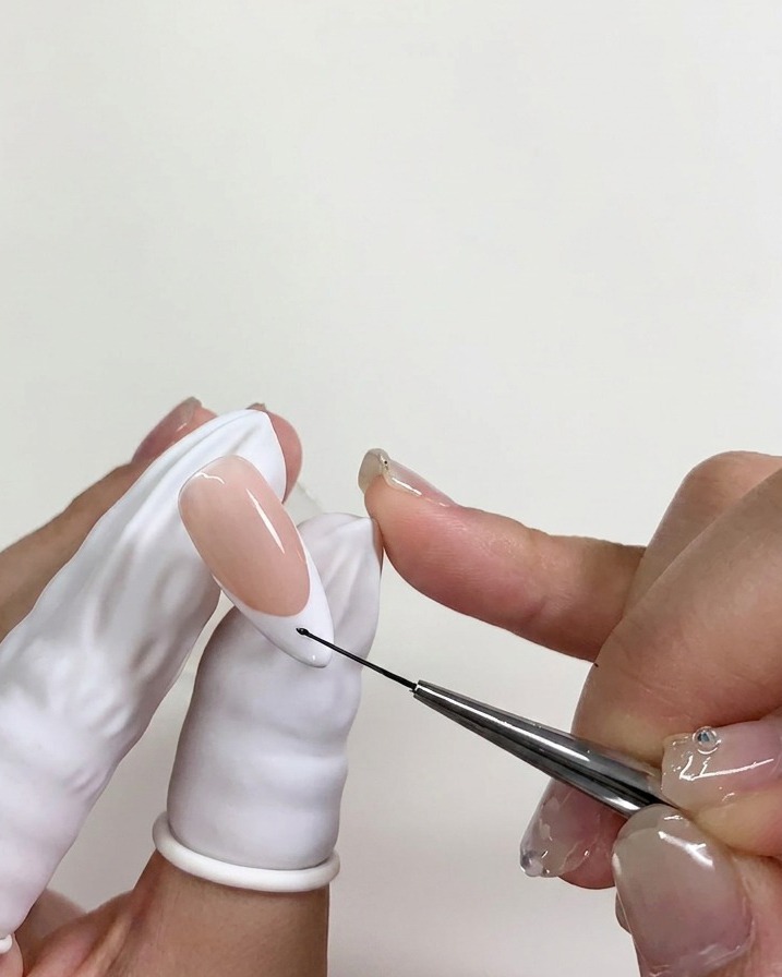 Un pinceau liner fin déposant un minuscule point de vernis gel noir sur la pointe de longle au-dessus du blooming gel humide.