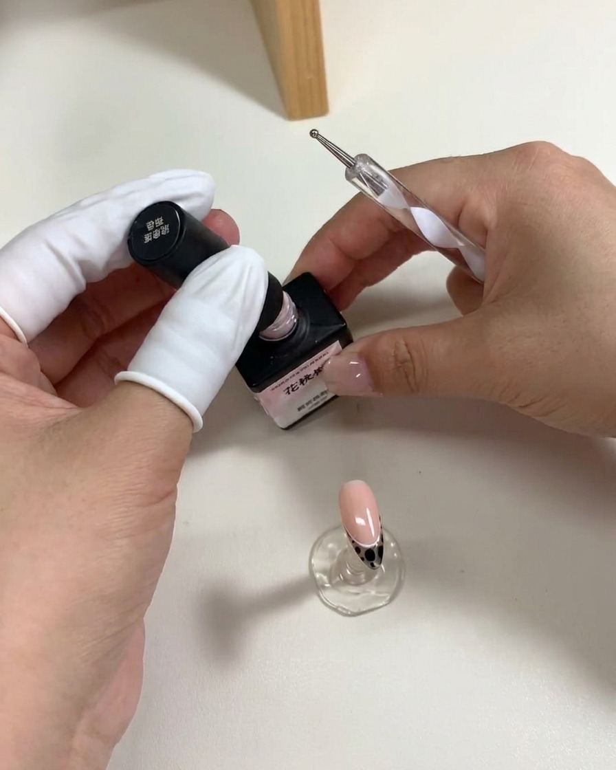 Un dotting tool déposant cinq points de gel rose sur la surface de longle pour former une fleur.