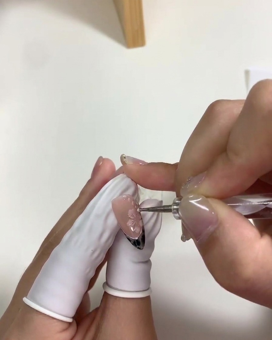 Gros plan dun dotting tool plaçant de petits points blancs autour des fleurs de cerisier sur un ongle.