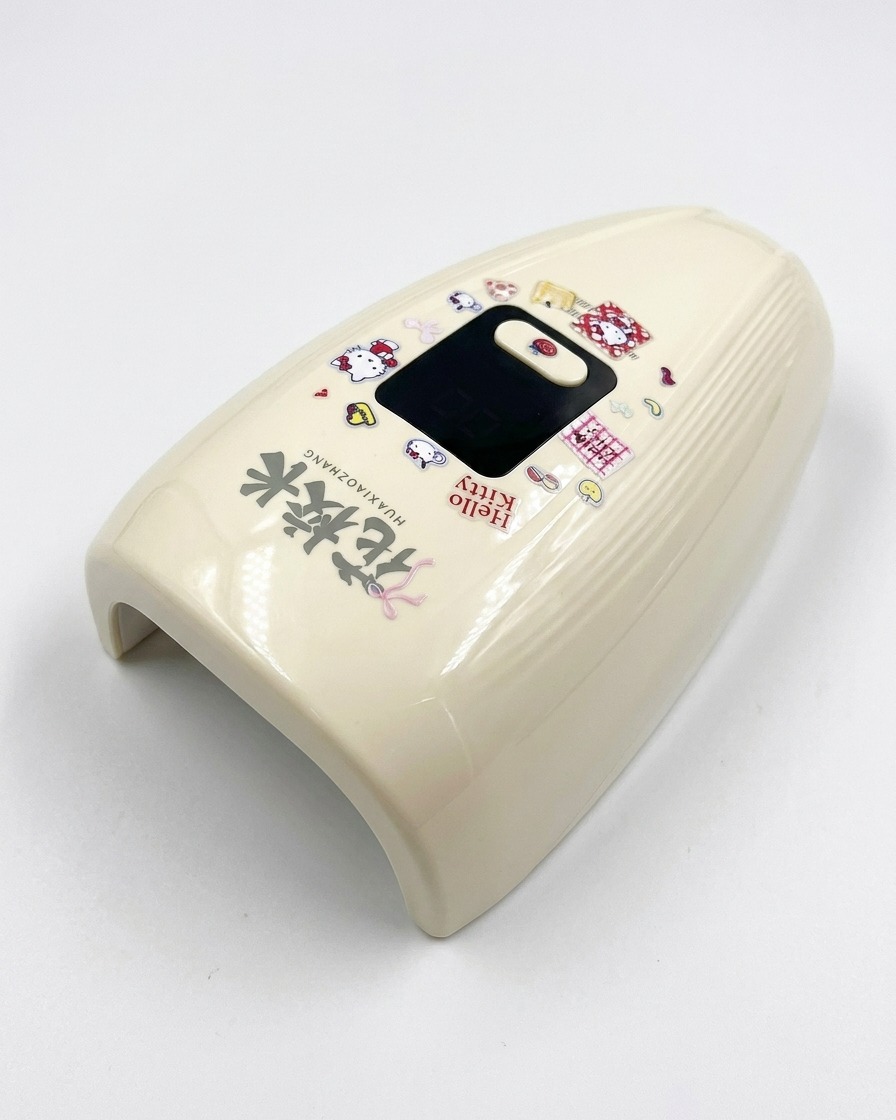 Une mini lampe UV/LED crème décorée dautocollants Hello Kitty sur une surface blanche.