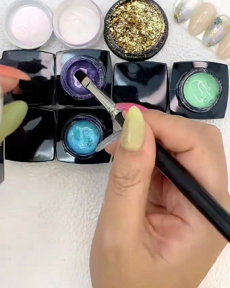 Un pinceau plaçant du gel violet aux côtés des gels bleu et vert sur un ongle.