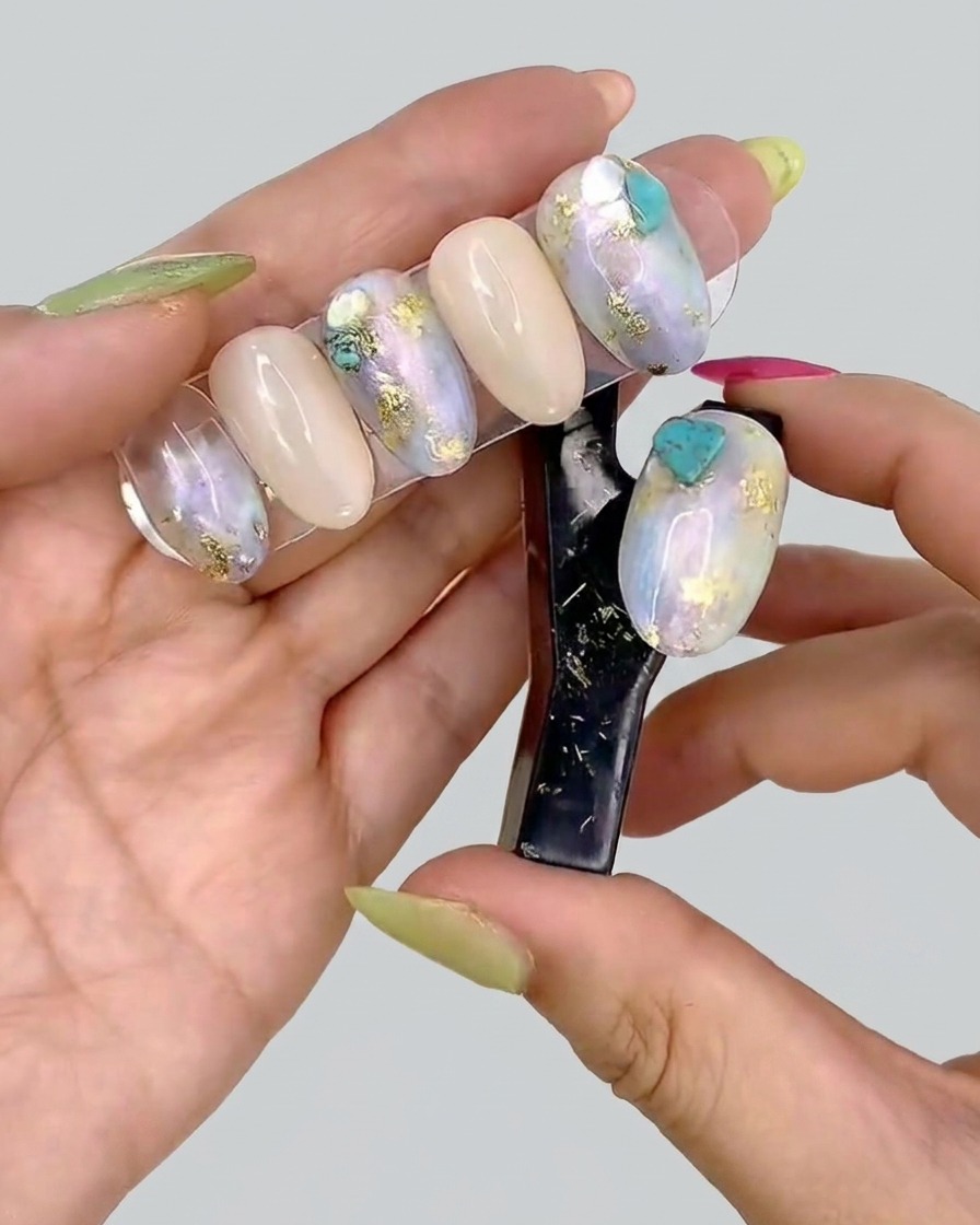 Une pince à épiler plaçant de petits morceaux délicats de feuille dor sur un ongle en gel décoré.