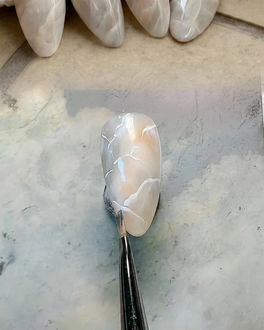 Petit pinceau rond propre estompant le bord dune ligne blanche sur un ongle marbré.