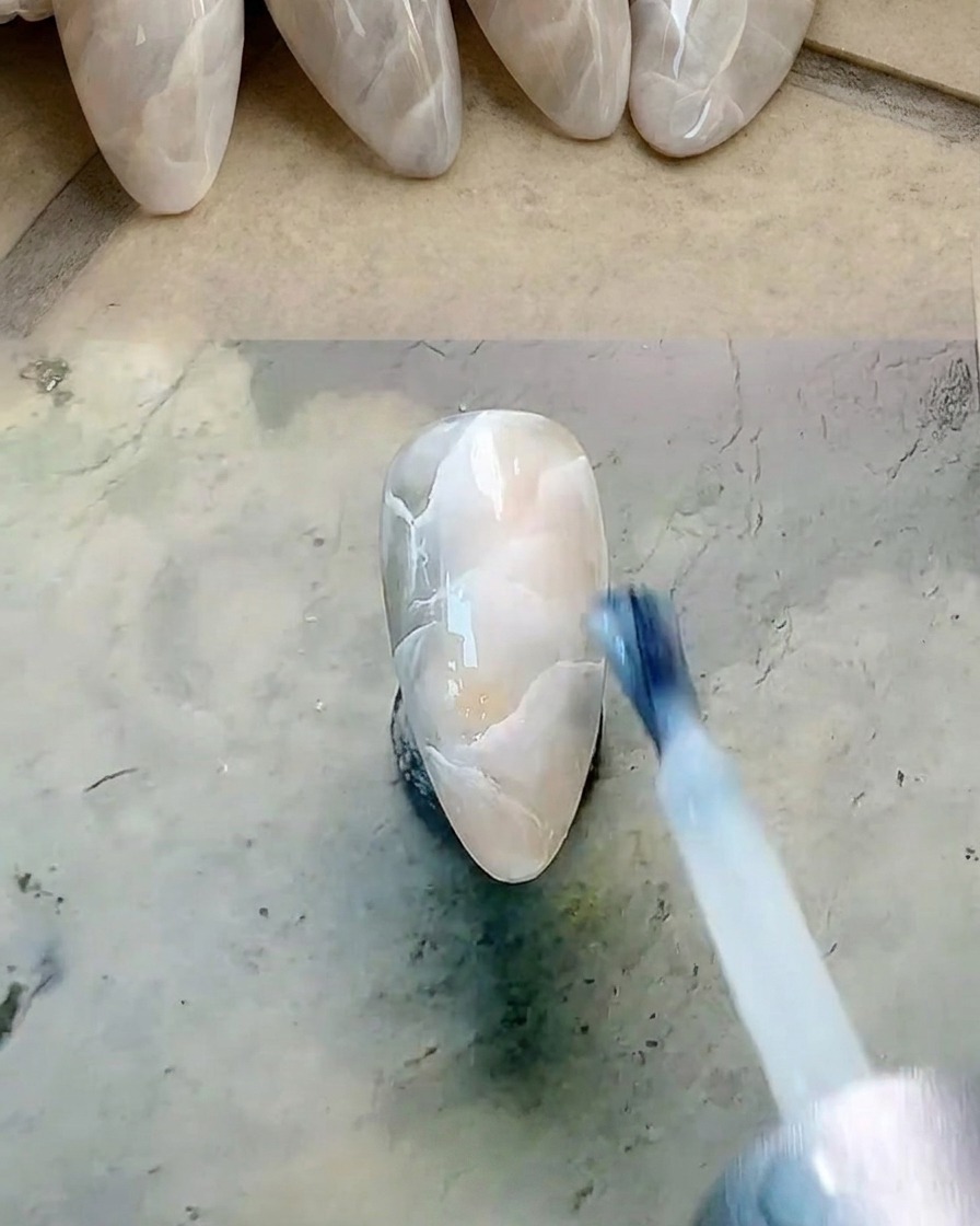 Pinceau plat appliquant une fine couche de gel blanc laiteux translucide sur longle marbré.