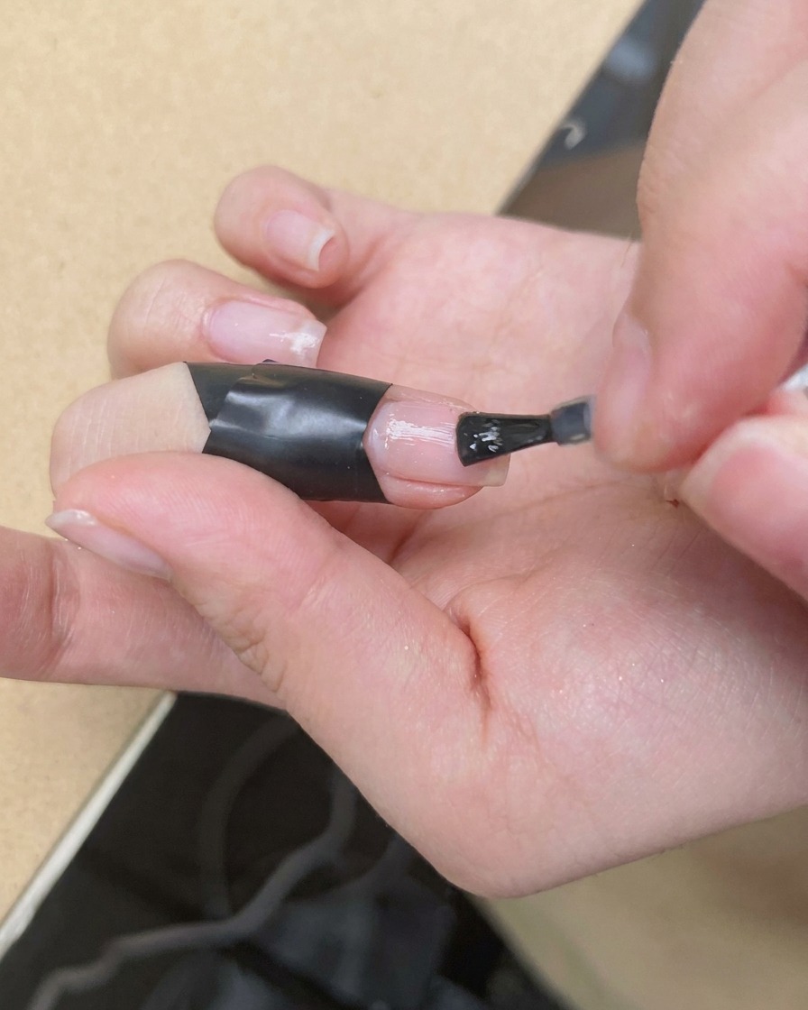 Un pinceau fin déposant une goutte de vernis rose vif au centre dun ongle recouvert de blooming gel humide.