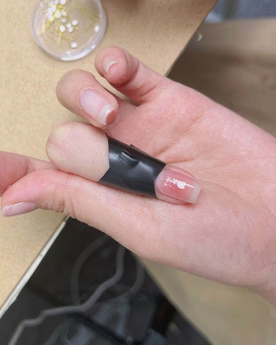 Une pince à épiler déposant un délicat ornement de fleur de cerisier blanche au centre dun ongle manucuré.