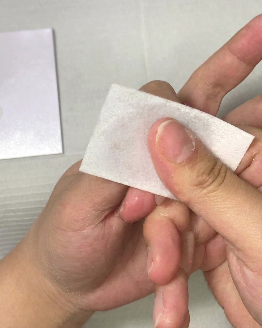 Gros plan dune main utilisant une lingette non pelucheuse pour nettoyer un ongle.