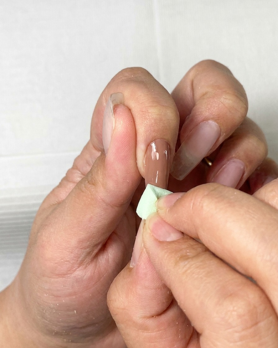 Un pinceau appliquant une fine couche de vernis gel marron sur un ongle naturel.