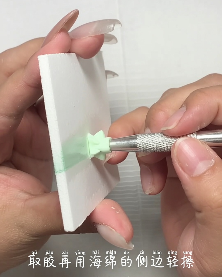 Vue rapprochée dun outil en métal appliquant une petite quantité de gel vernis vert clair depuis une palette sur le bord dune éponge.