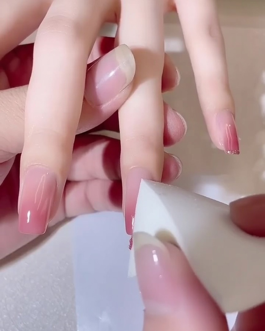 Gros plan dune éponge tapotant sur un ongle, montrant un effet de dégradé rose qui sintensifie.