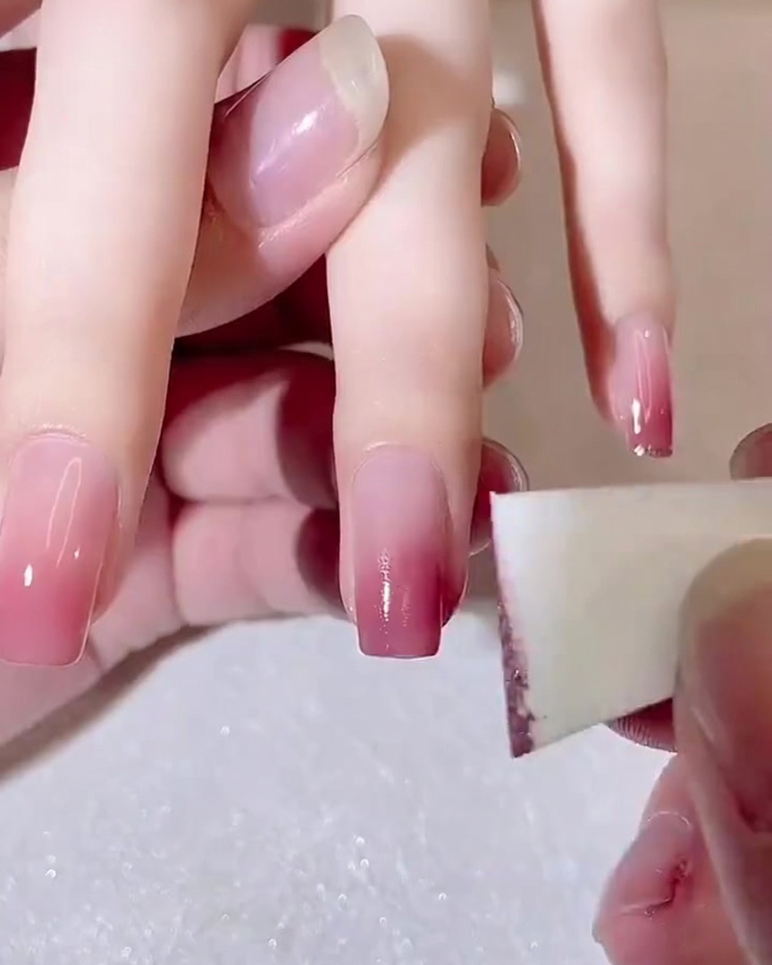 Vue rapprochée dune éponge à maquillage utilisée pour tapoter une deuxième couche de gel rose foncé sur la pointe dun ongle.