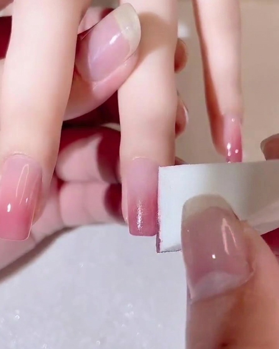 Une éponge estompant doucement la transition de couleur sur un ongle.