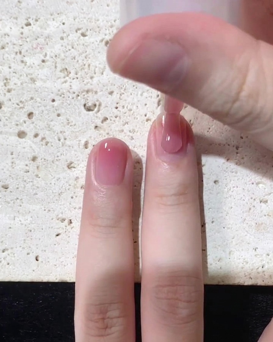 Gros plan sur un pinceau appliquant un vernis gelée rose transparent près de la cuticule