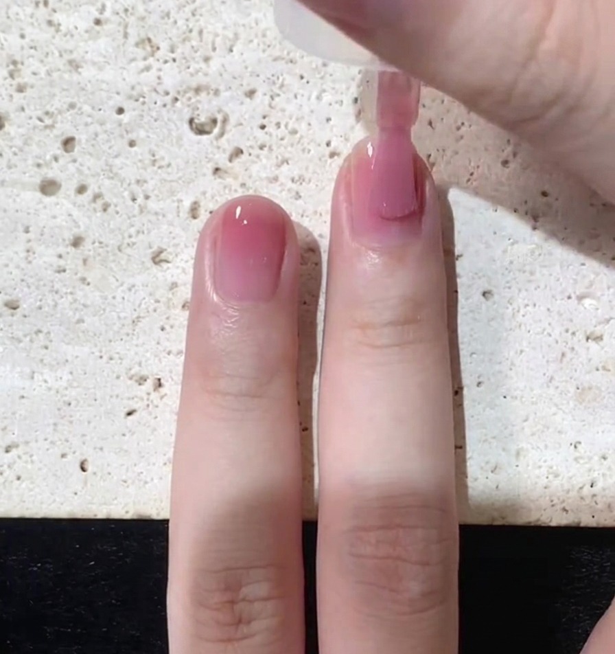 Gros plan sur un pinceau appliquant une fine couche de vernis rose translucide sur un ongle naturel