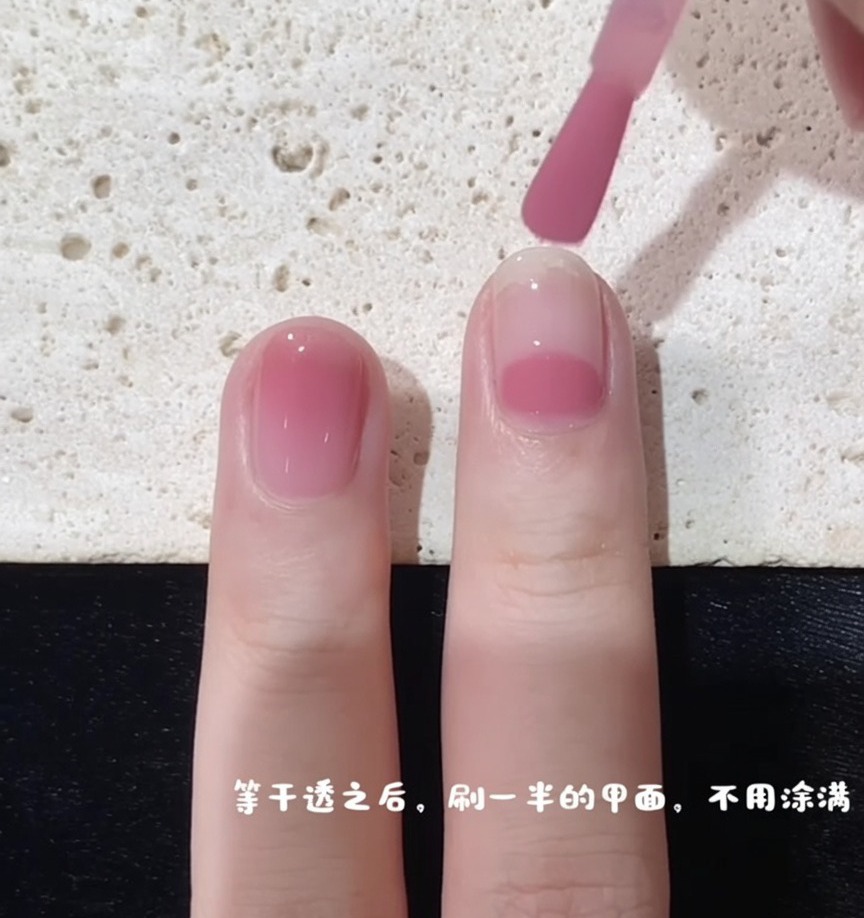 Un pinceau commençant lapplication de vernis rose au milieu de longle pour créer leffet dégradé