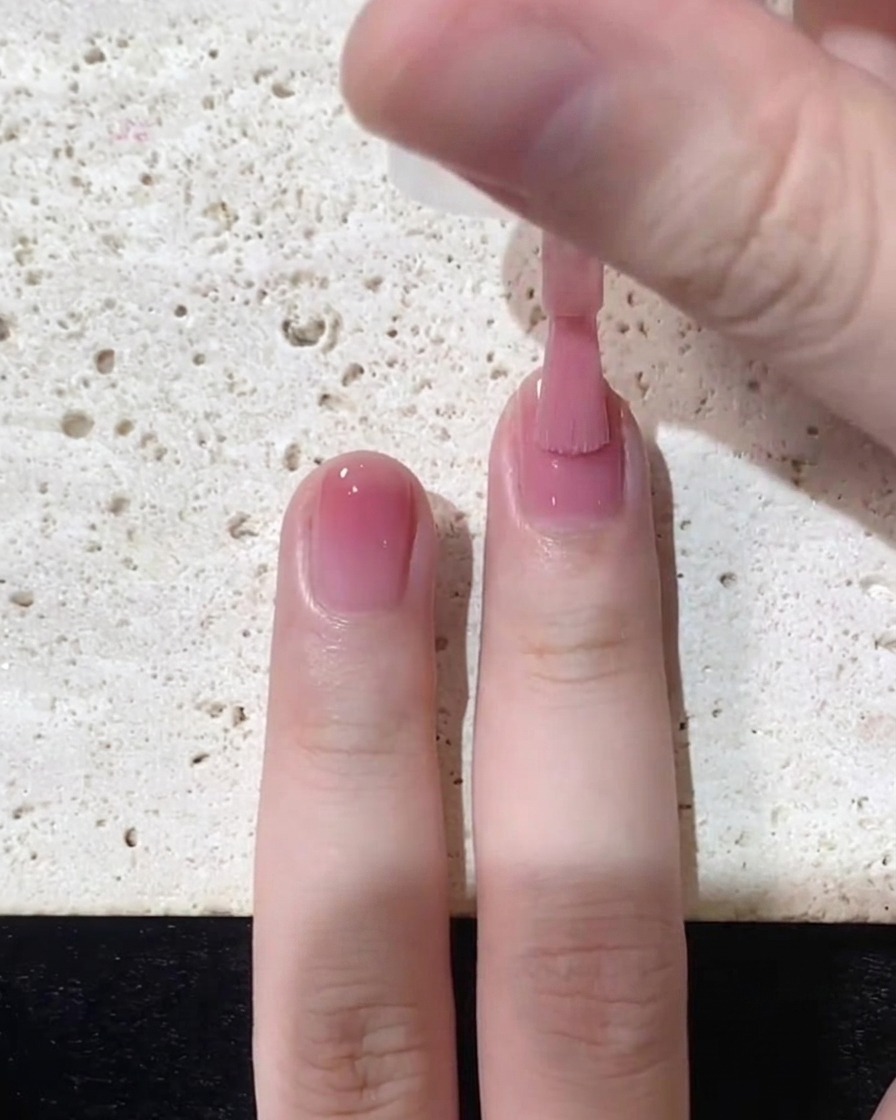 Un pinceau étirant le vernis rose gelée vers le bord libre sur la moitié supérieure de longle