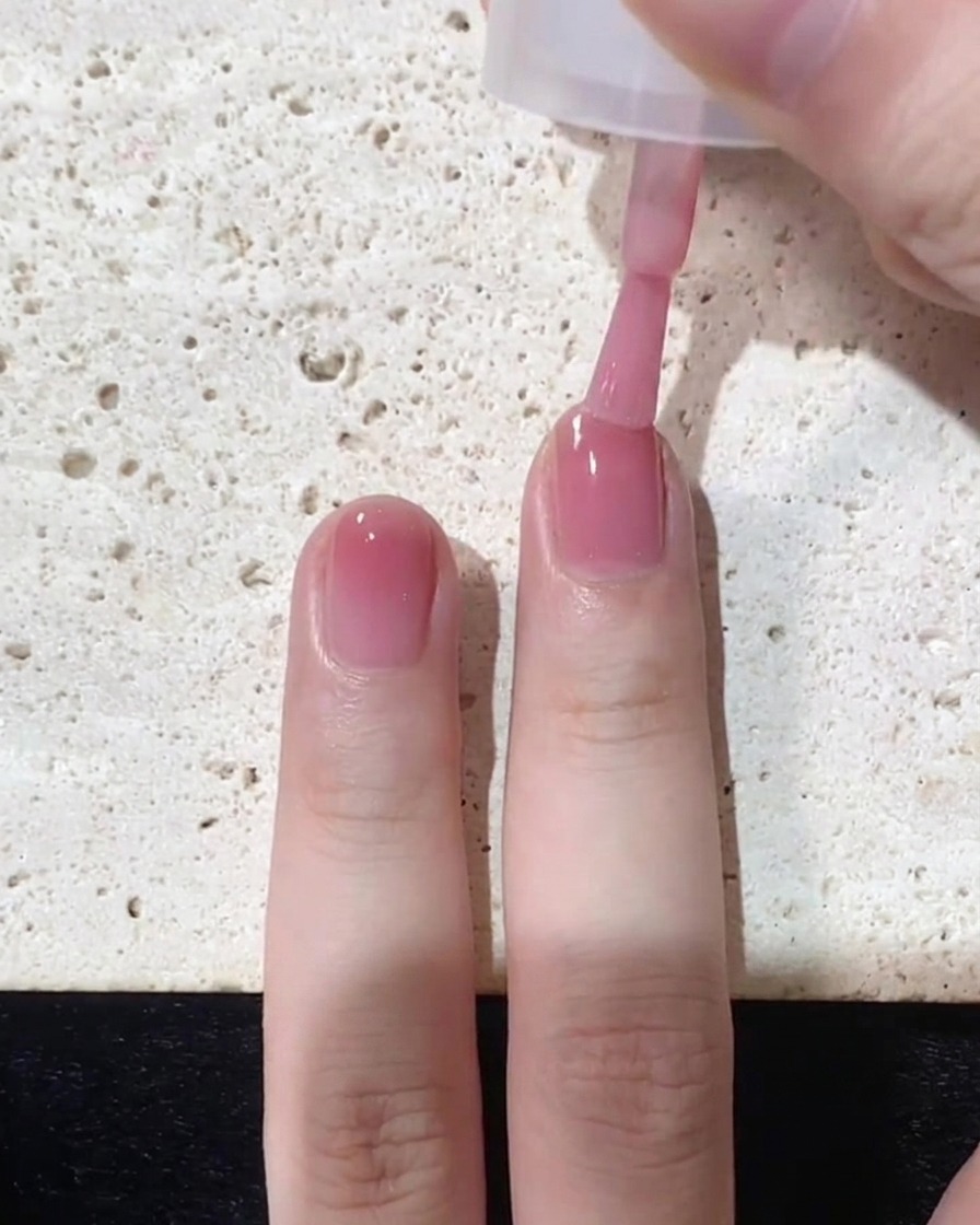 Un pinceau appliquant une couche finale concentrée de vernis rose spécifiquement sur le bout de longle