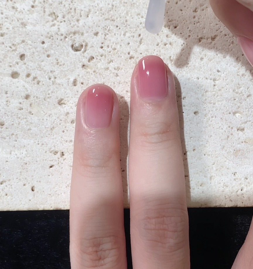 Un pinceau appliquant un top coat transparent et brillant sur longle dégradé terminé