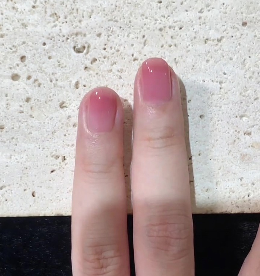 Gros plan sur lapplication finale du top coat lissant un ongle dégradé rose