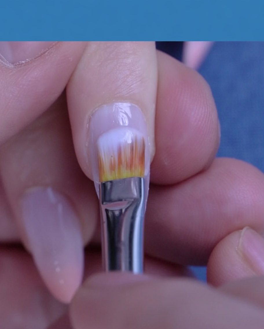 Un pinceau appliquant un vernis gel blanc laiteux translucide sur un ongle naturel.
