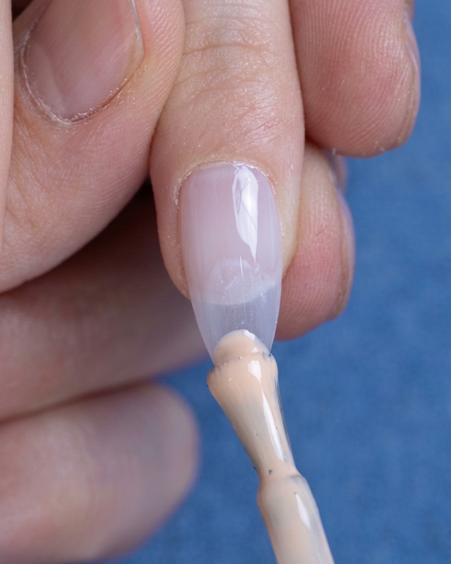 Une petite perle de vernis gel nude appliquée sur le bord libre de longle.