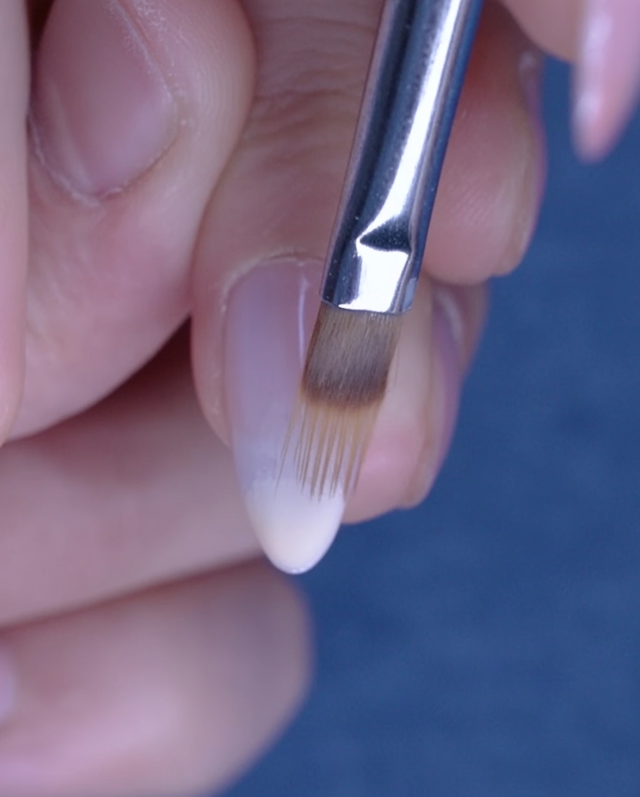 Un pinceau plat estompant le gel nude vers le haut de longle pour créer un effet ombré.