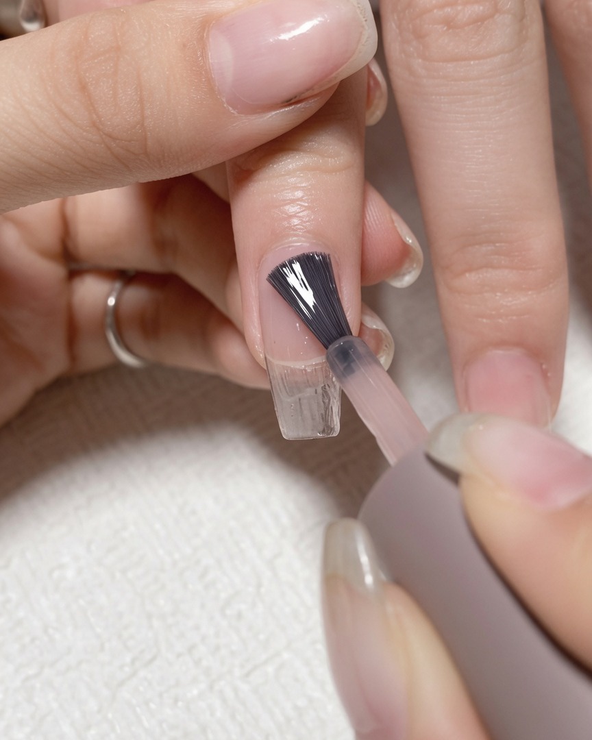 Un pinceau appliquant un gel de base transparent sur un ongle naturel propre.