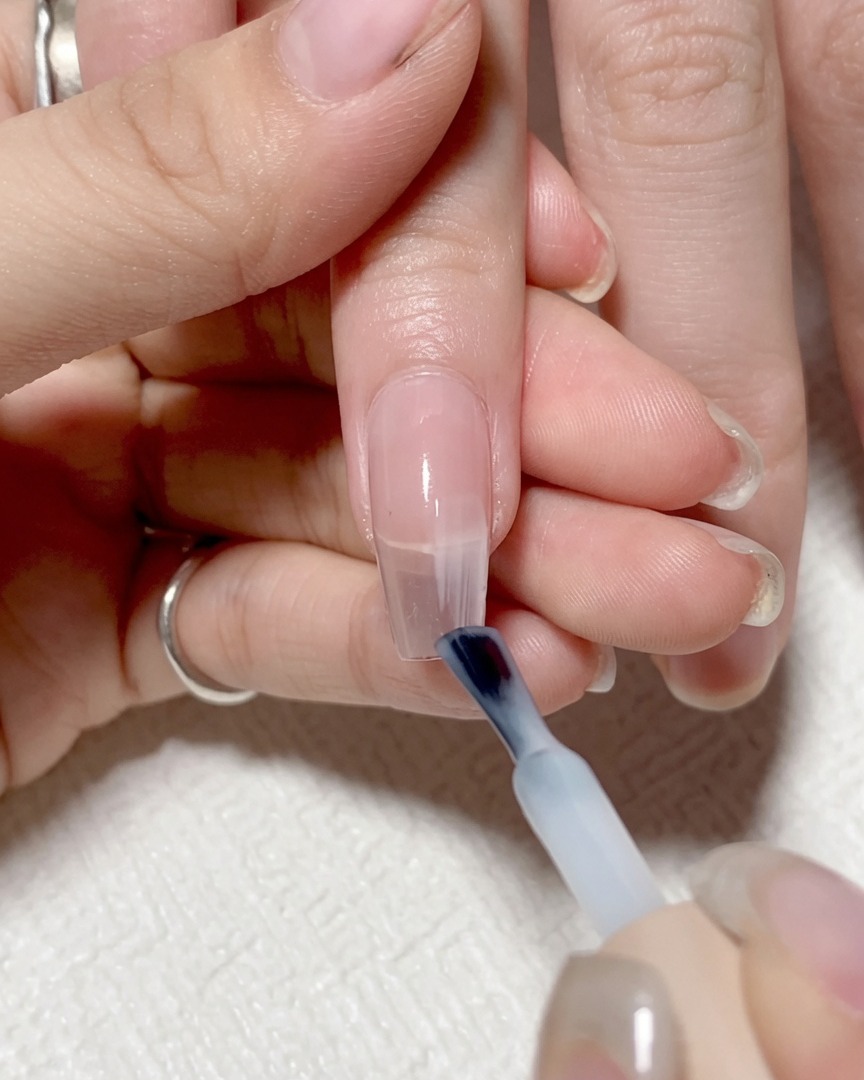 Un pinceau à ongles appliquant un gel clair et léger sur la partie droite de longle.