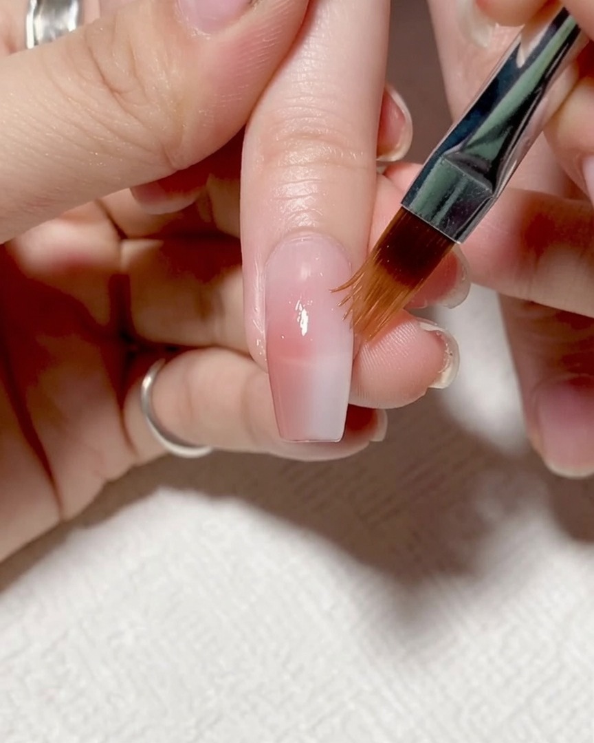 Application dun gel renforçateur clair sur toute la surface de longle.