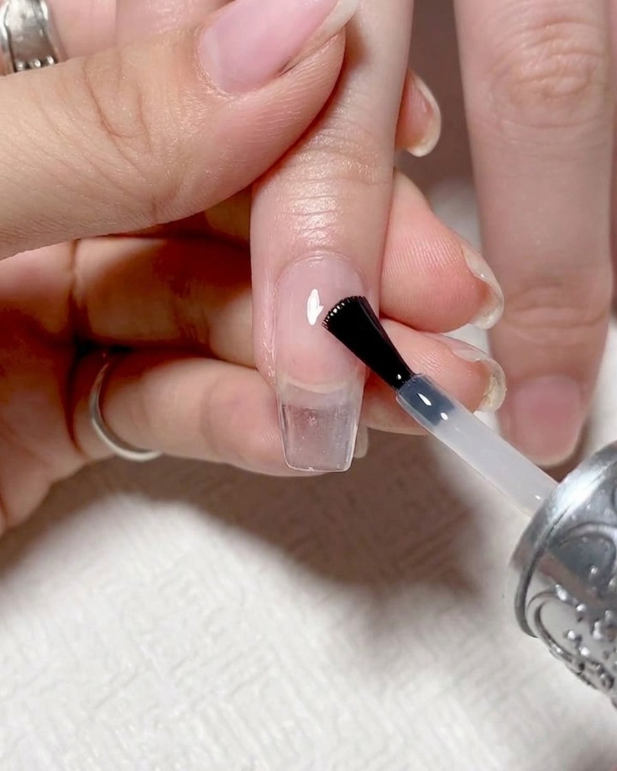 Application dun top coat brillant sur un ongle déjà ombré.