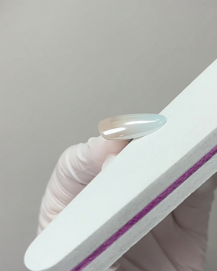 Une lime à ongles touchant légèrement le bord libre dun ongle fini chromé pour enlever lexcès de pigment.