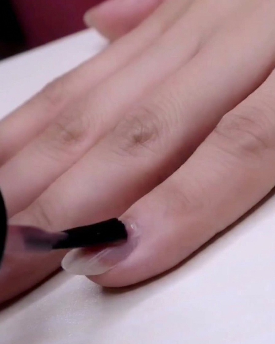 Un pinceau appliquant un vernis jelly rose transparent sur tout longle du petit doigt.