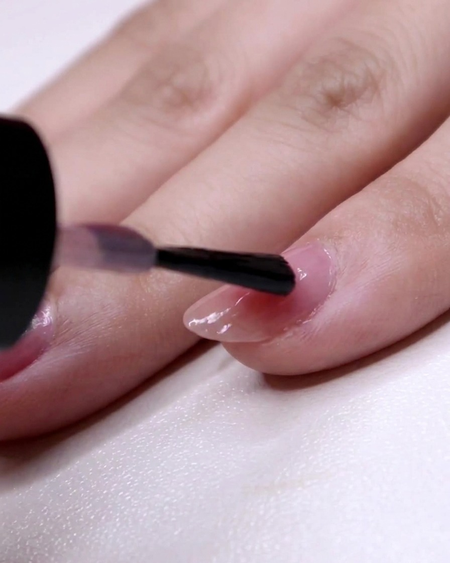 Un pinceau à ongles peignant la deuxième couche de vernis rose à partir de la position des deux tiers jusquà la pointe de lannulaire.